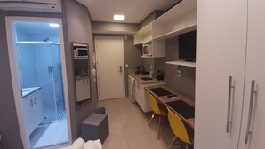 A compact kitchen with a microwave, sink, and a small dining area with yellow chairs. - 123 Quarto - Sé (São Paulo)