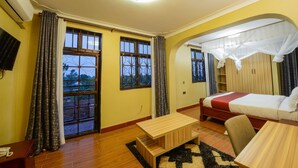 Habitación de hotel con cama, escritorio, silla, televisor y ventana con cortinas.