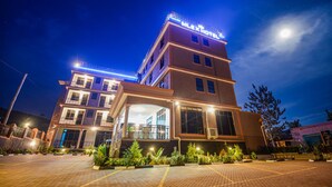 Un hotel de varios pisos con un letrero llamativo, un acceso cubierto y un área exterior bien iluminada con plantas.