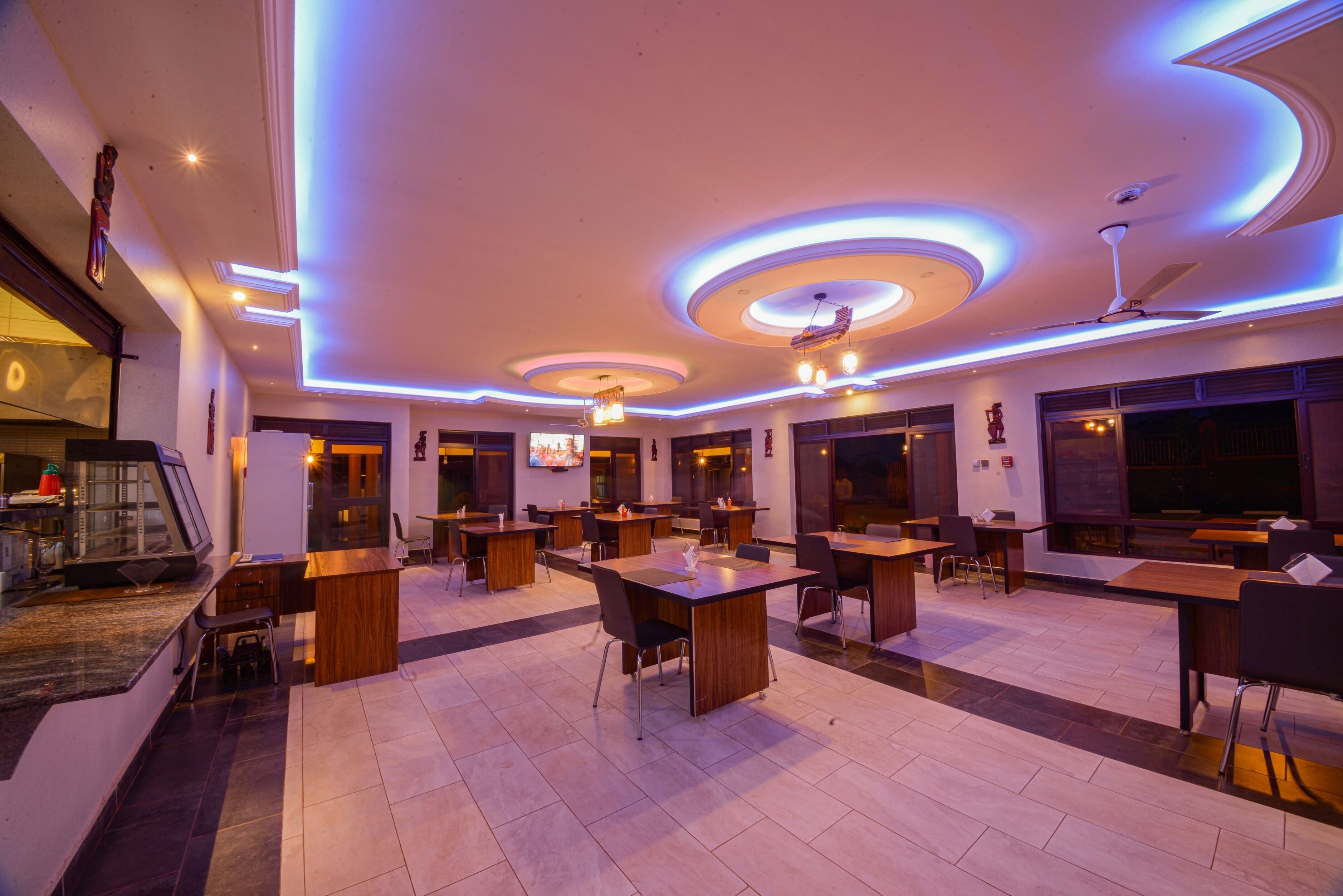 A spacious dining area with multiple tables and chairs, a ceiling with circular light fixtures, and a television mounted on the wall.