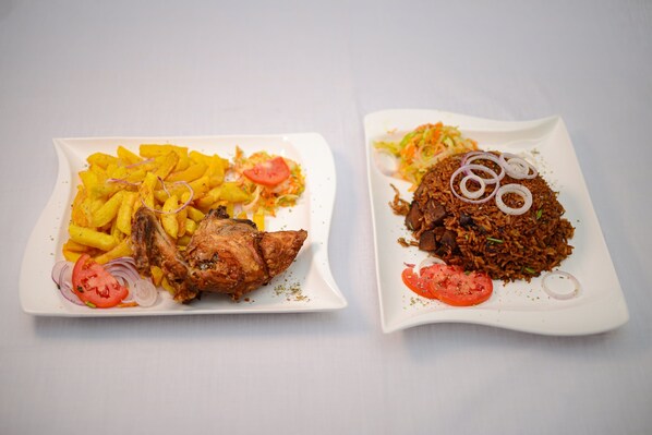 Two square white plates with food. One plate has a fried fish and fries, and the other has a rice dish with onions and tomatoes. - Mlex Hotel (Maya)