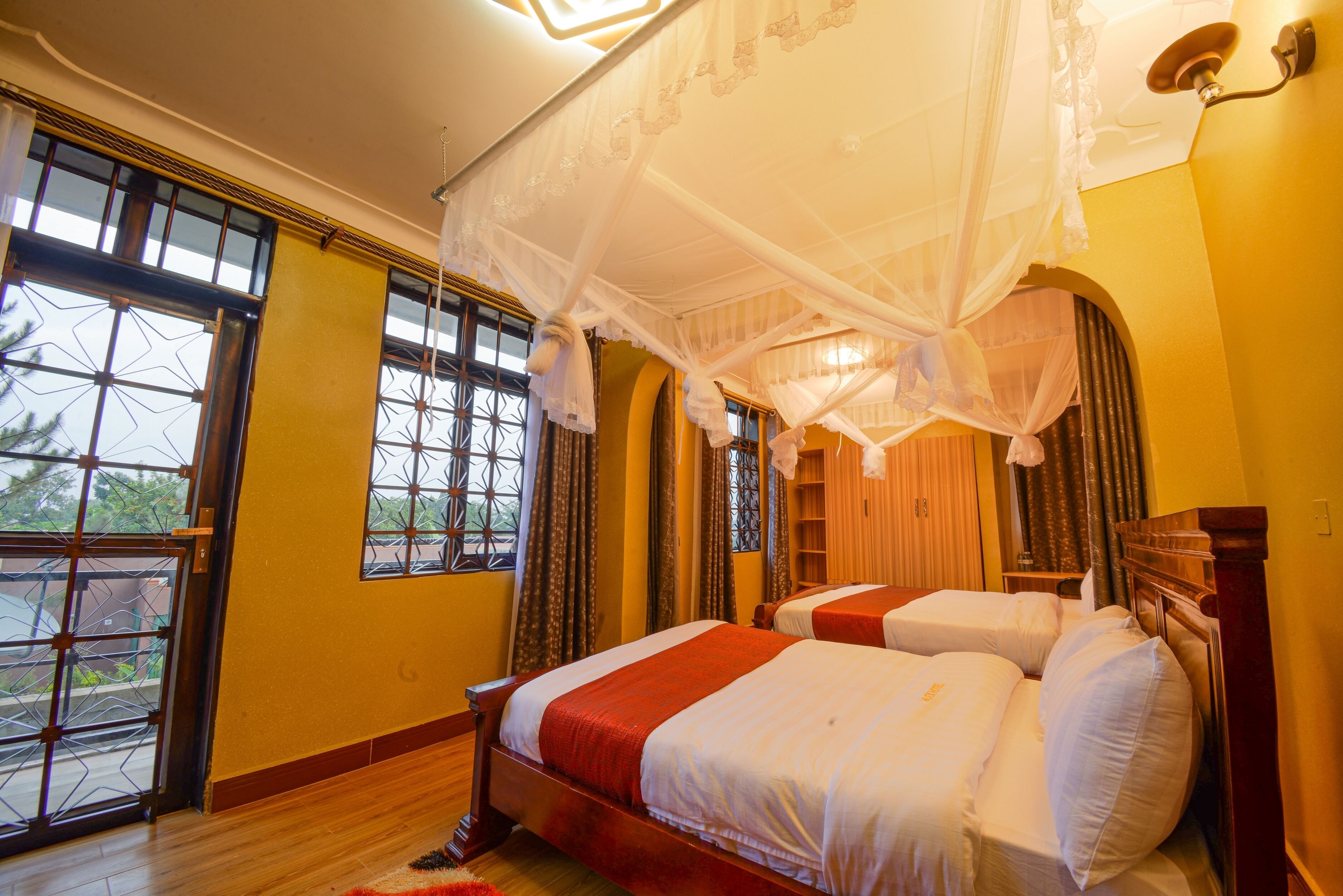 A hotel room with two beds, a large window with a view, and a canopy bed.