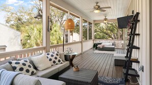 Une véranda couverte avec une terrasse en bois, des sièges d’extérieur, des ventilateurs de plafond et un téléviseur fixé au mur.