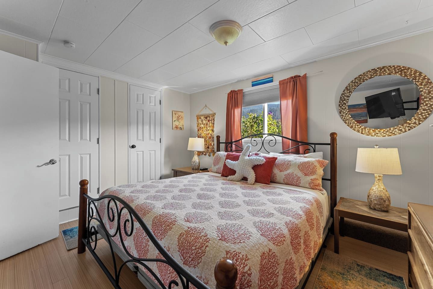 Une chambre à coucher avec un lit, deux tables de chevet, un miroir rond et une fenêtre avec des rideaux.