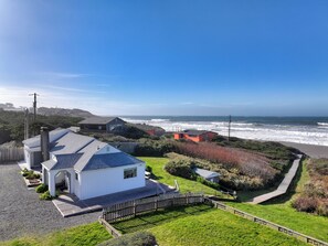 A coastal property with a white building, a wooden deck, and a view of the ocean. - Beach House @ Spirit Cove- Beach Path & SPA (Gold Beach)
