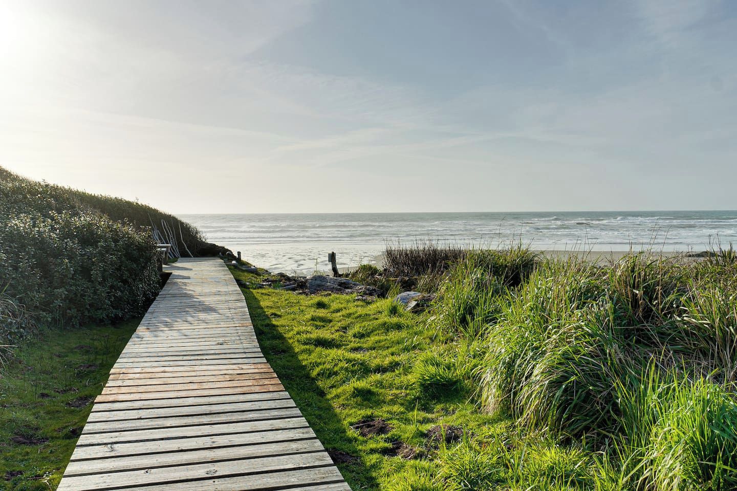 Een houten looppad dat naar een strand leidt, met grasvelden aan weerszijden.