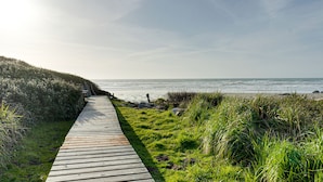 Une promenade en bois qui mène à une plage bordée de zones herbeuses et offrant une vue dégagée sur l’océan.