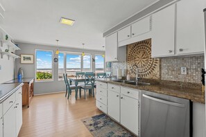 A modern kitchen with white cabinets, a granite countertop, and a view of the outdoors. - Beach House @ Spirit Cove- Beach Path & SPA (Gold Beach)
