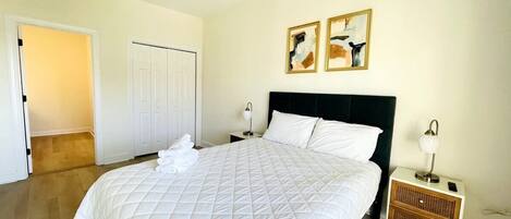 A bedroom with a large bed, a ceiling fan, a nightstand with a lamp, and two framed artworks on the wall.