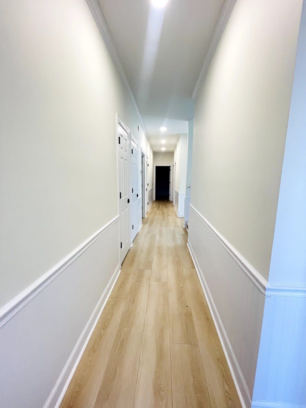 Un long couloir étroit, doté d’un plancher en bois et de murs blancs.