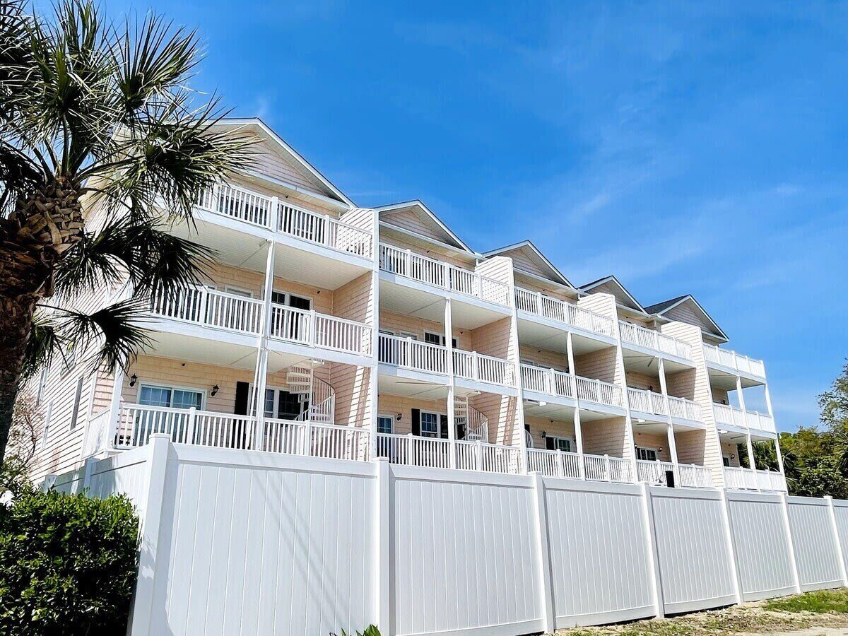 A multi-story hotel with balconies, white railings, and a white fence.