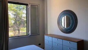 Un dormitorio con cama, cómoda, ventana con cortinas y espejo adosado a la pared.