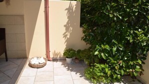 Un patio empedrado con una planta en maceta, una cesta y un tubo fijado a la pared.