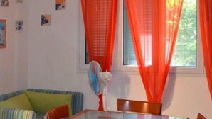 Una habitación con un sofá a rayas, una mesa, un ventilador y una ventana con cortinas rojas.