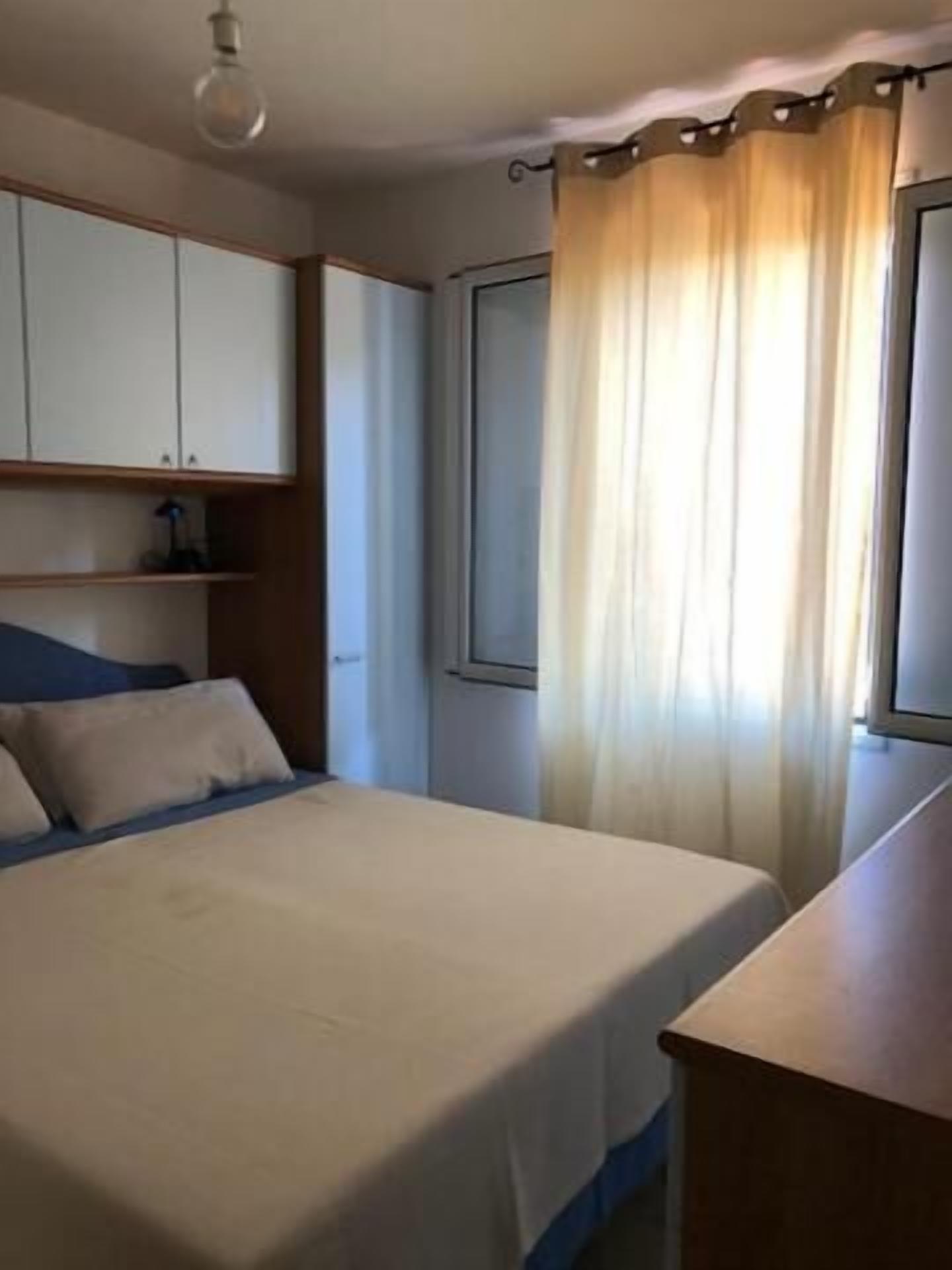 A bedroom with a bed, a nightstand, a wardrobe, and a window with curtains.