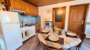 A compact kitchen with wooden cabinets, a white refrigerator, a microwave, and a dining table set for four.