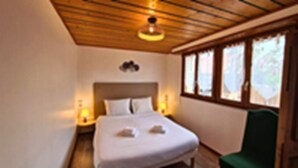 A bedroom with a bed, a green chair, and a window with curtains. - Erable – Large Holiday Cottage – Terrace & Parking | Near Colmar and Kaysersberg (Beblenheim)