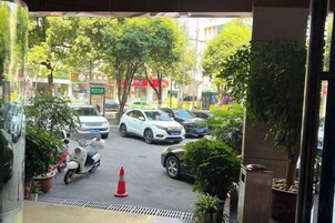 A parking area with cars and a scooter, surrounded by potted plants and trees.