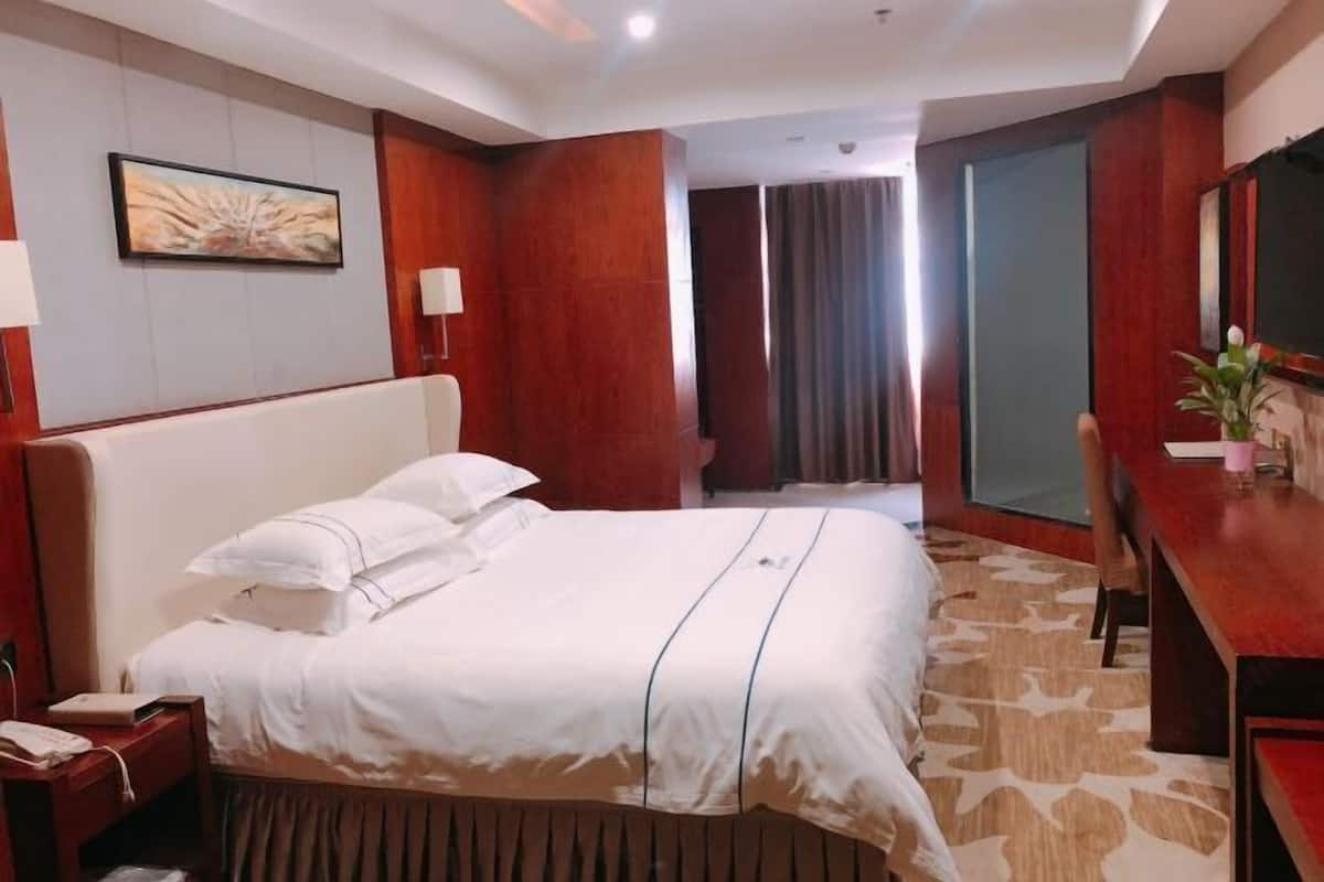 A hotel room with a bed, bedside table, lamp, and a painting on the wall.