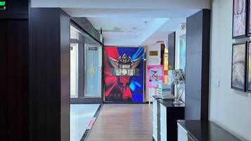 Pasillo de hotel con pantalla digital, obras de arte enmarcadas y un mostrador de recepción.