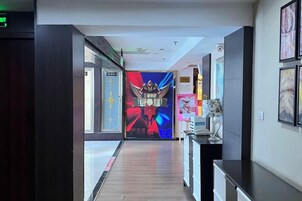 Pasillo de hotel con pantalla digital, obras de arte enmarcadas y un mostrador de recepción.