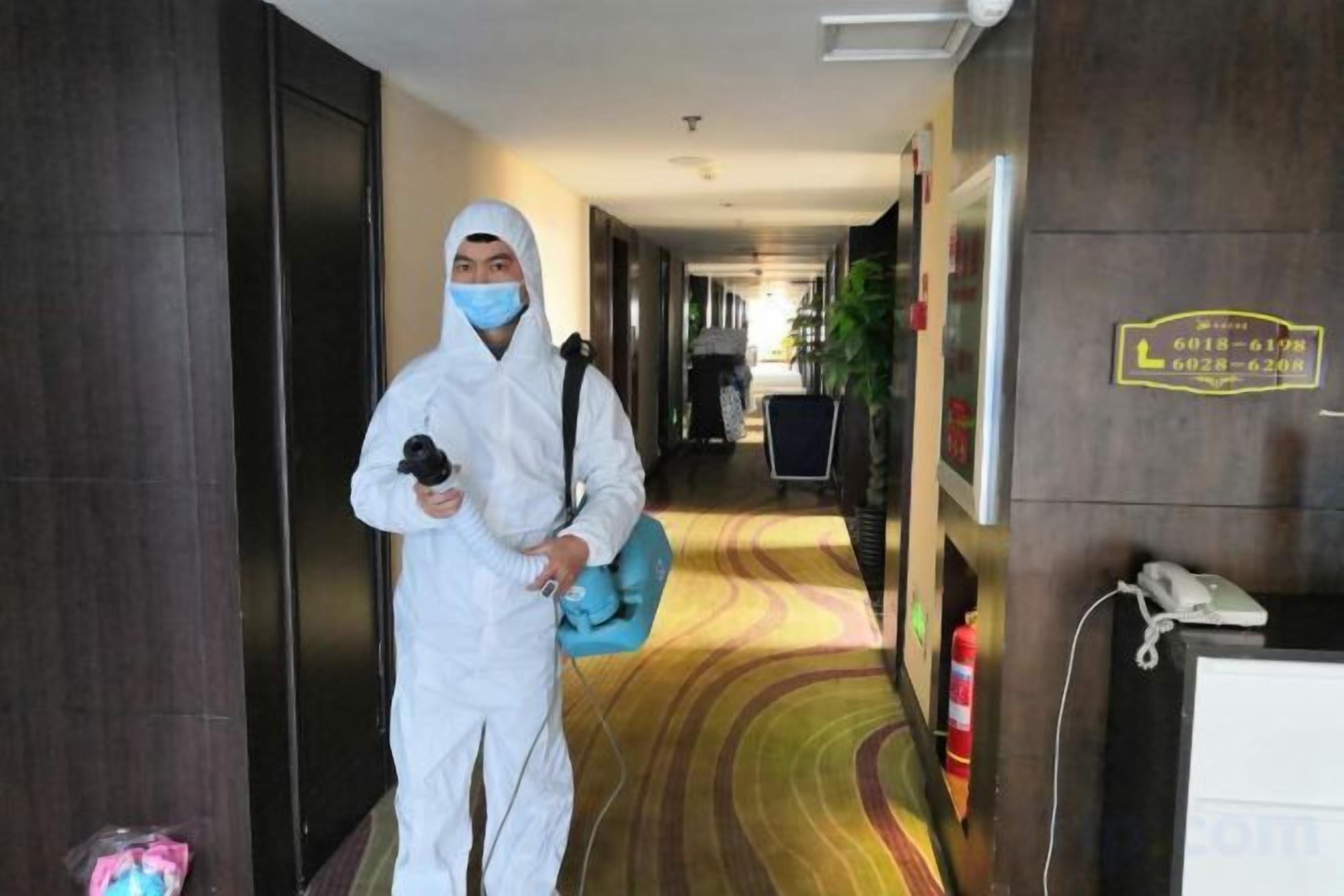 A hotel corridor with a reception desk, a fire extinguisher, and a sign indicating room numbers.