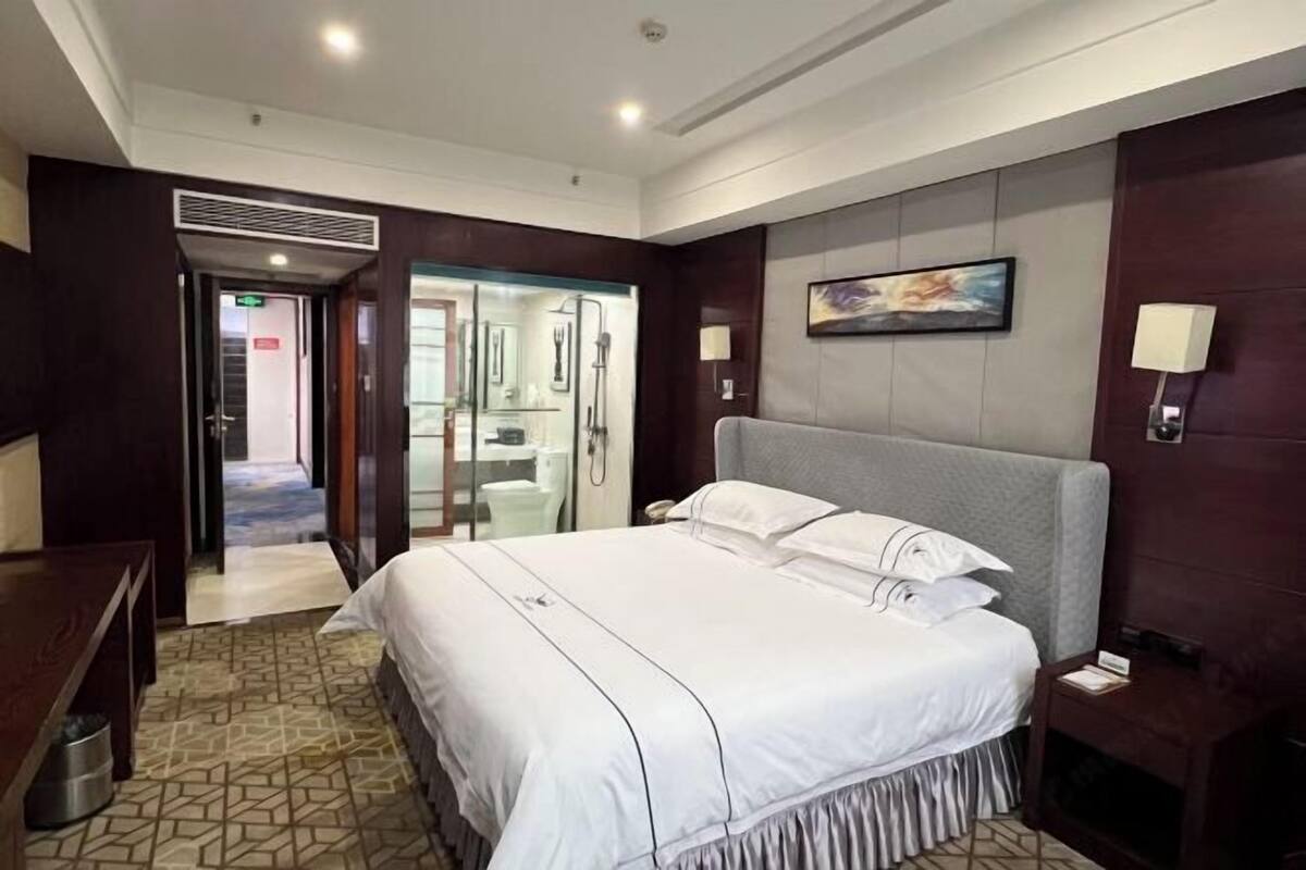 A hotel room with a large bed, a desk, a chair, a nightstand, a lamp, and a painting on the wall.