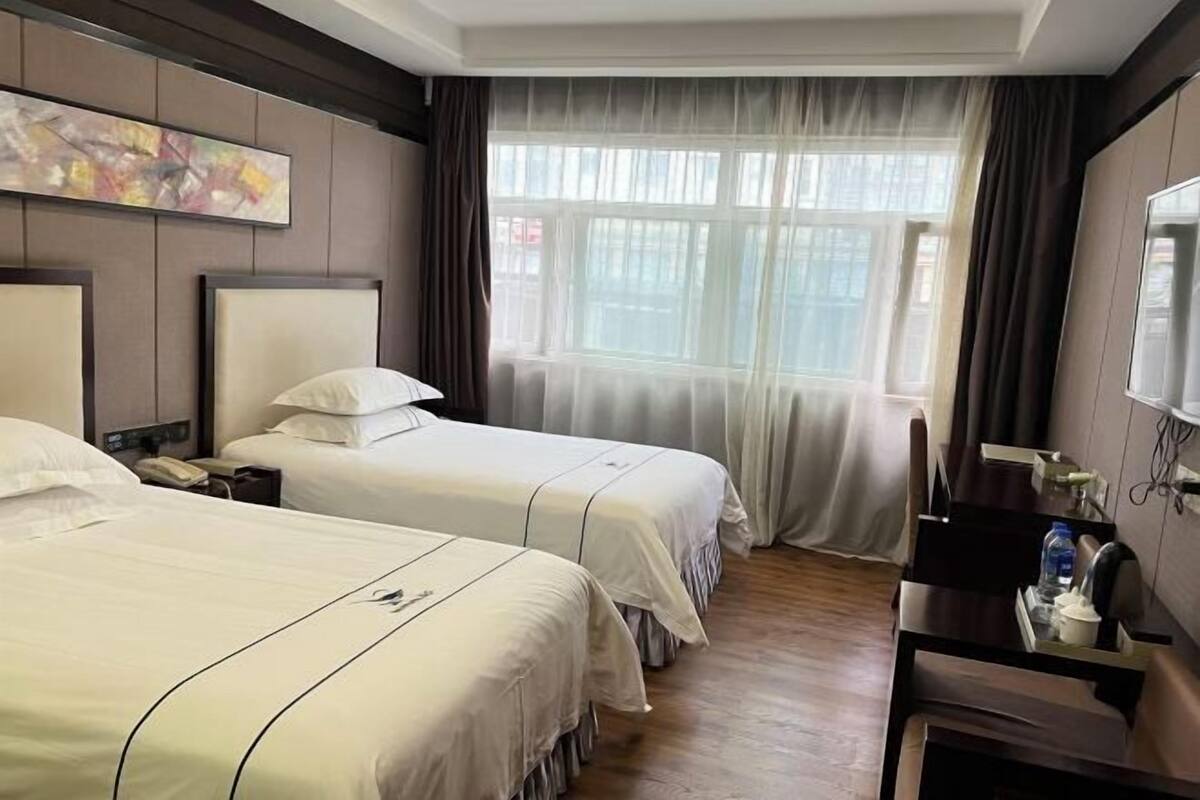 A hotel room with two beds, a desk, a chair, a telephone, and a window with curtains.
