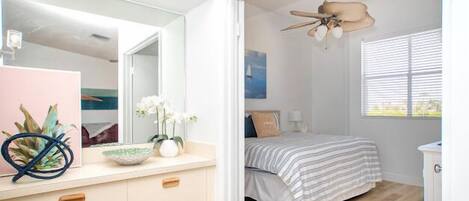 Un dormitorio con una cama, un ventilador de techo, una ventana con persianas, una mesita de noche y un aparador.