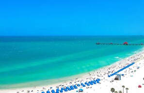A beach with a pier extending into the ocean, a sandy shore, and numerous umbrellas. - Beautiful Golf course views minutes from St. Pete Beach (St. Petersburg)