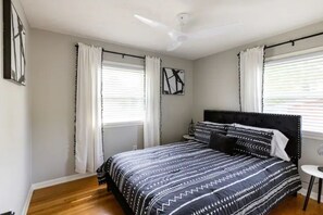 Une chambre à coucher avec un lit, des rideaux, un ventilateur de plafond et un tableau encadré au mur.