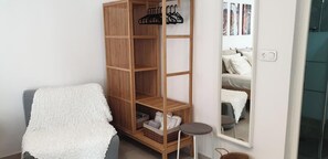 A room with a wooden wardrobe, a mirror, a grey sofa, and a small round table.