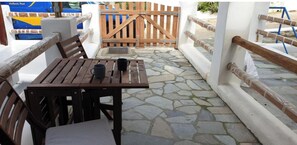 A wooden table with chairs and a bench, a stone-tiled floor, and a wooden gate in the background.