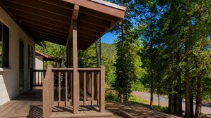 Un patio in legno con un portico coperto, gradini in pietra e vista su una zona boschiva.