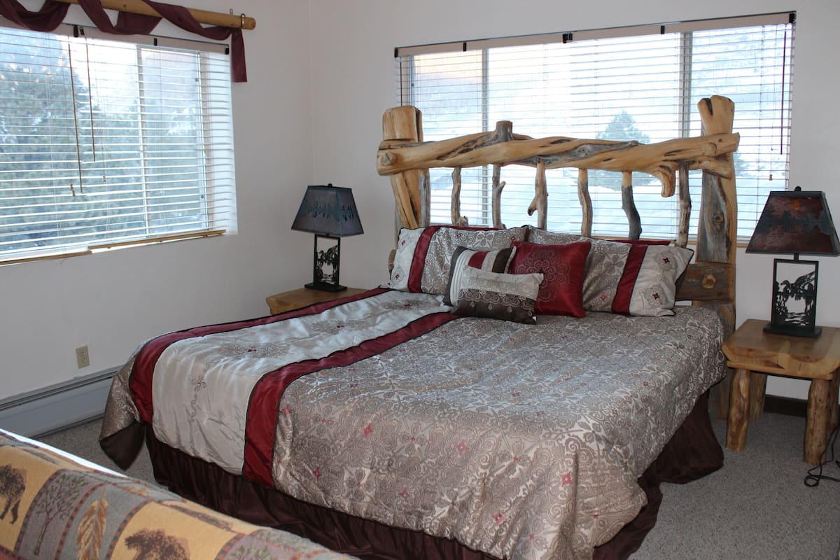 A bedroom with a large bed, two bedside tables, and a window with blinds.