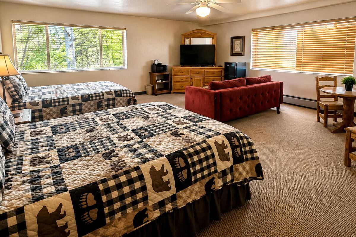 A bedroom with two beds, a red sofa, a TV, and a ceiling fan.