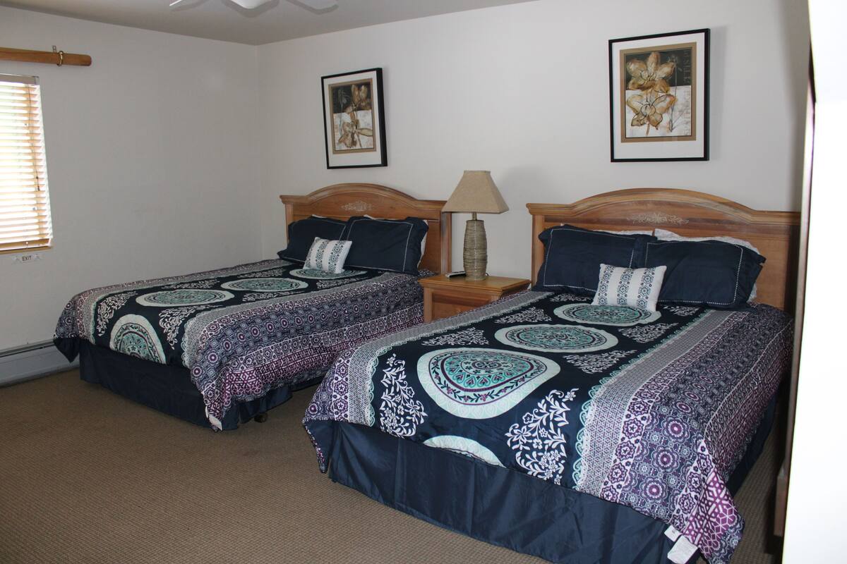 A bedroom with two single beds, each with a patterned bedspread, a wooden headboard, and a nightstand with a lamp.