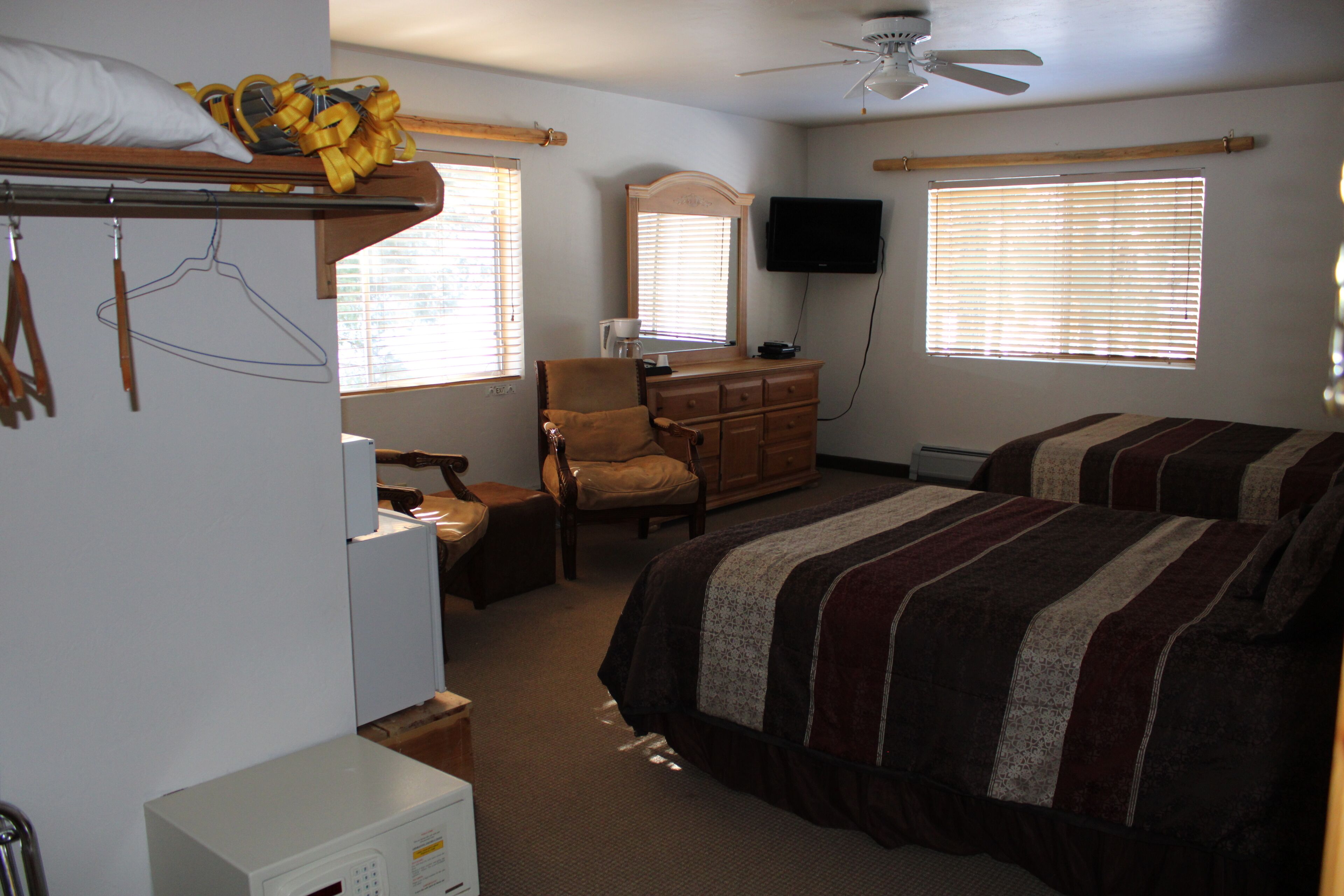 Une chambre avec deux lits, une commode, une chaise, un bureau, un téléviseur et un ventilateur de plafond.