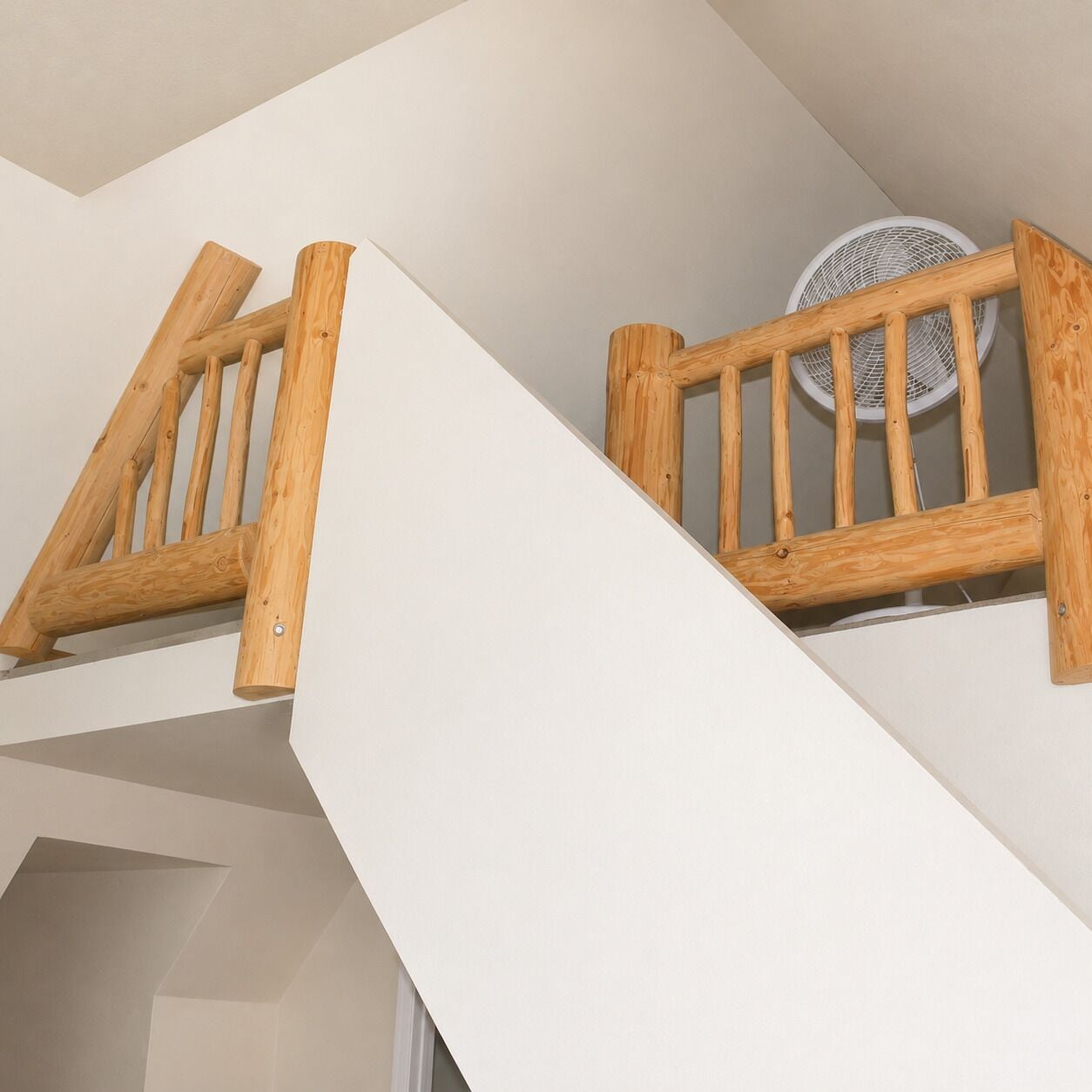 A wooden staircase with a white wall and a ceiling fan.