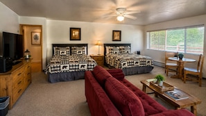 A room with two beds, a red sofa, a wooden table, a TV, and a window with blinds. - Edelweiss Resort and Restaurant (Greer)