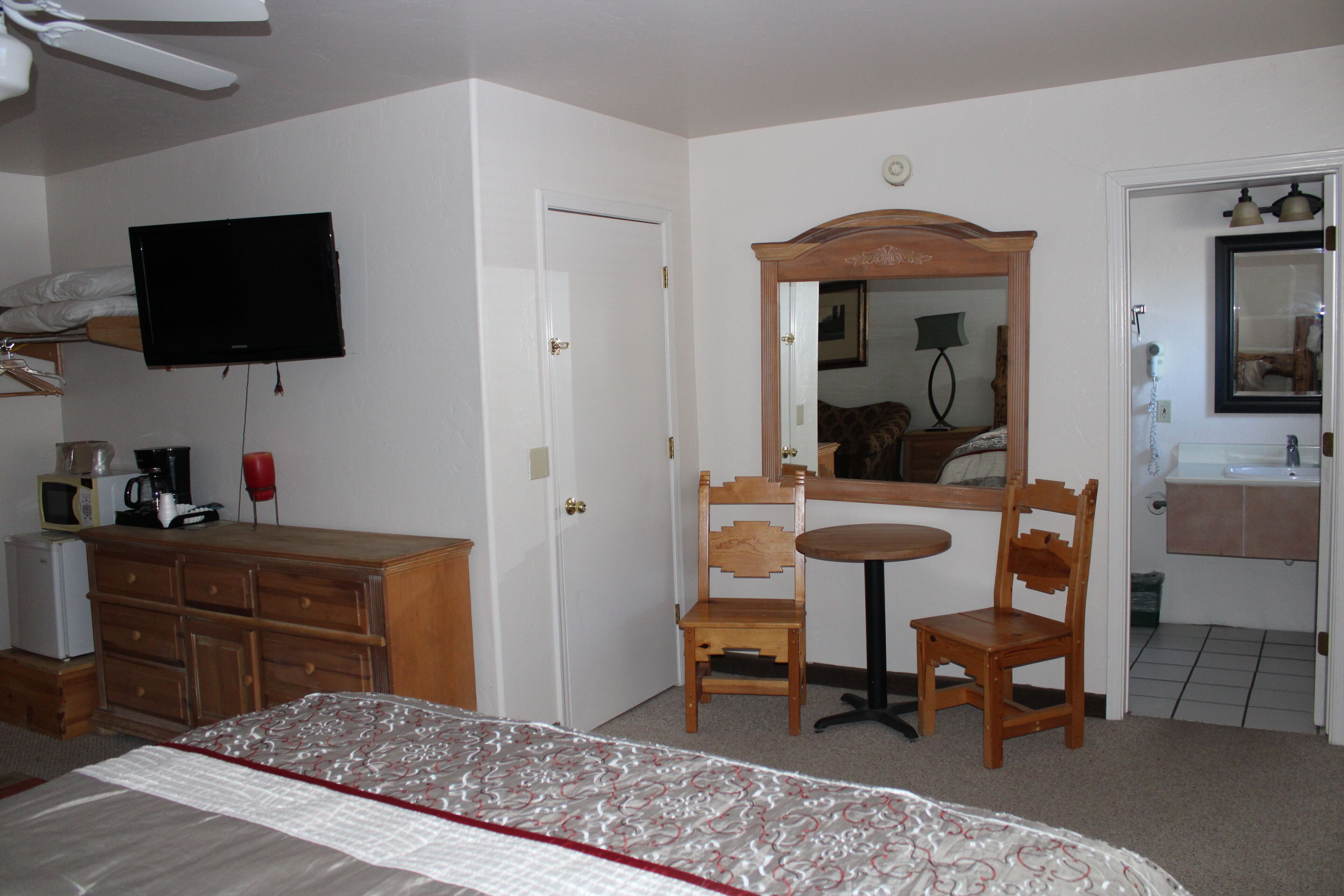 A hotel room with a bed, a television, a wooden dresser, a mirror, and a bathroom visible through an open door.