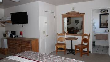 A hotel room with a bed, a television, a wooden dresser, a mirror, and a bathroom visible through an open door.