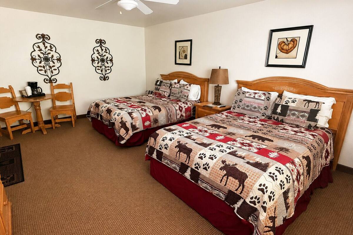 A room with two beds, a ceiling fan, a table with chairs, and wall decorations.