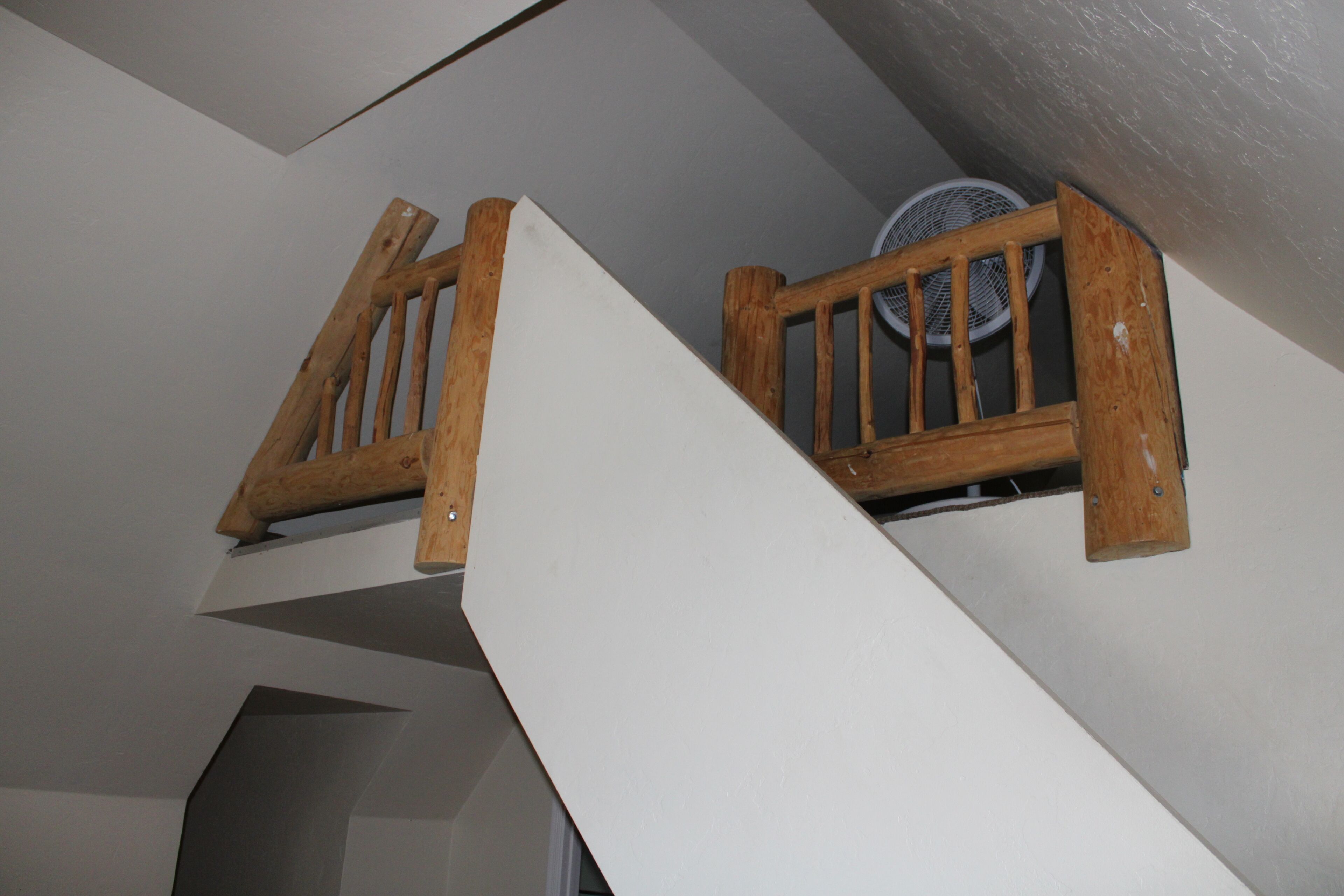 Una escalera de madera con una pared blanca y un ventilador de techo.