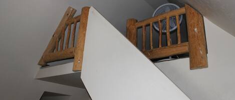 Una escalera de madera con una pared blanca y un ventilador de techo.