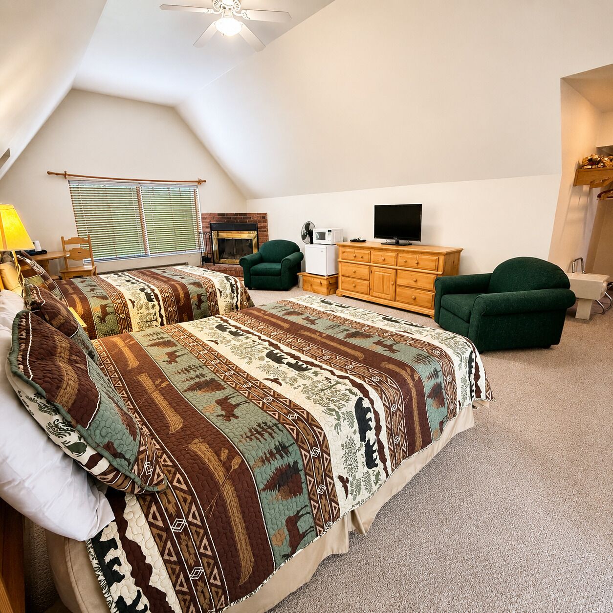 Une chambre à coucher avec un grand lit, deux fauteuils verts, une commode en bois, un téléviseur et une cheminée.