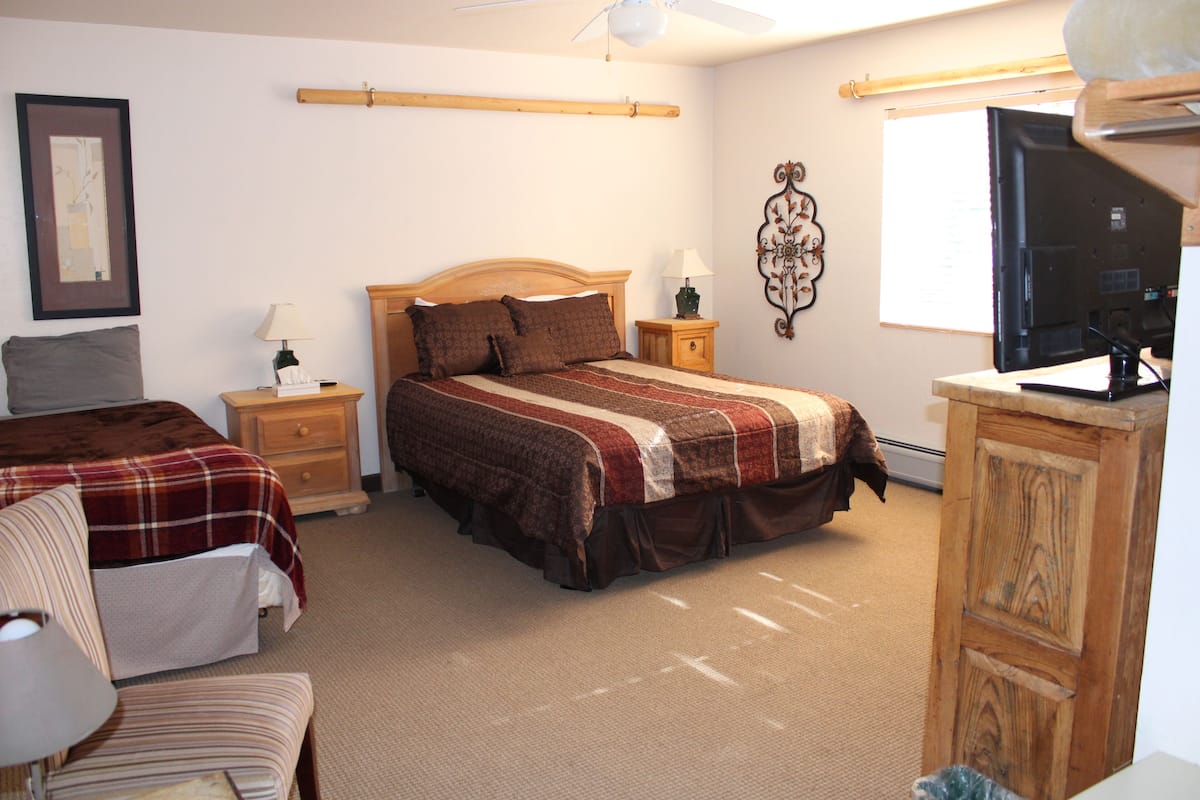 A bedroom with a bed, bedside tables, a chair, a TV, and a wardrobe.