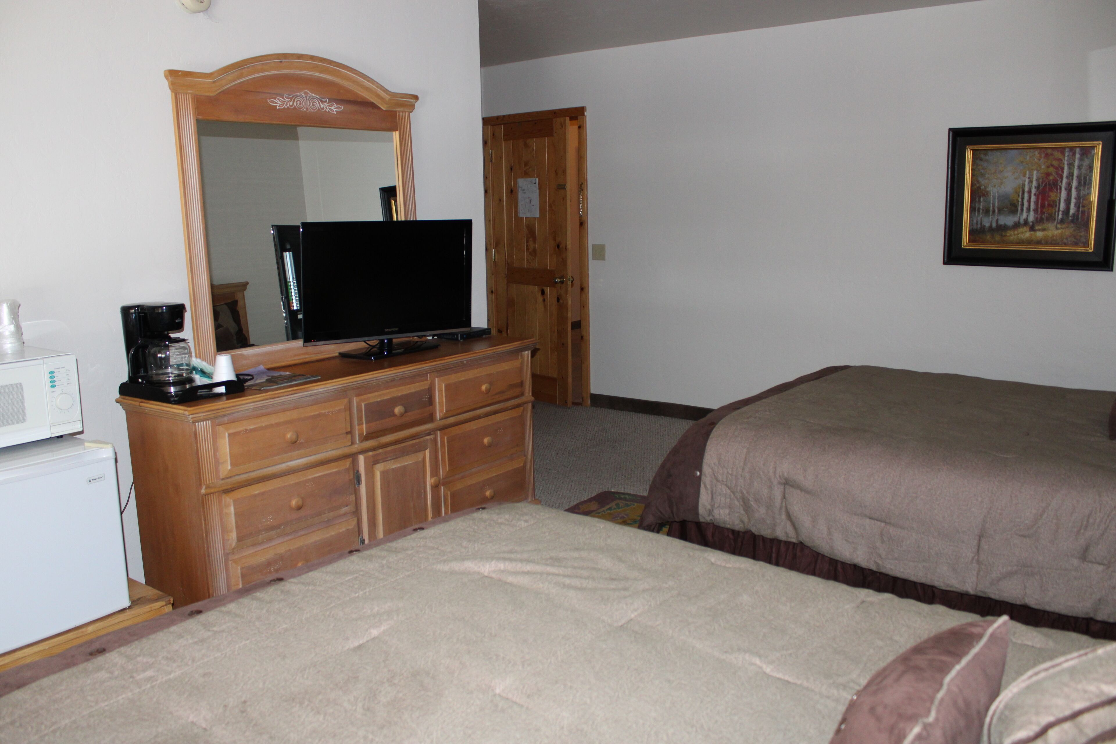 Een slaapkamer met een houten dressoir, een flatscreen-tv, een bed met een bruine plaid en een schilderij aan de muur.