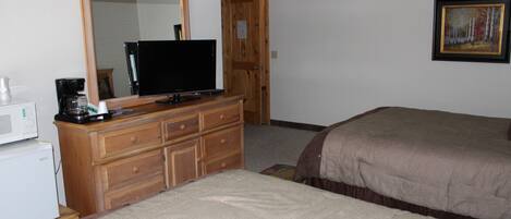 Een slaapkamer met een houten dressoir, een flatscreen-tv, een bed met een bruine plaid en een schilderij aan de muur.