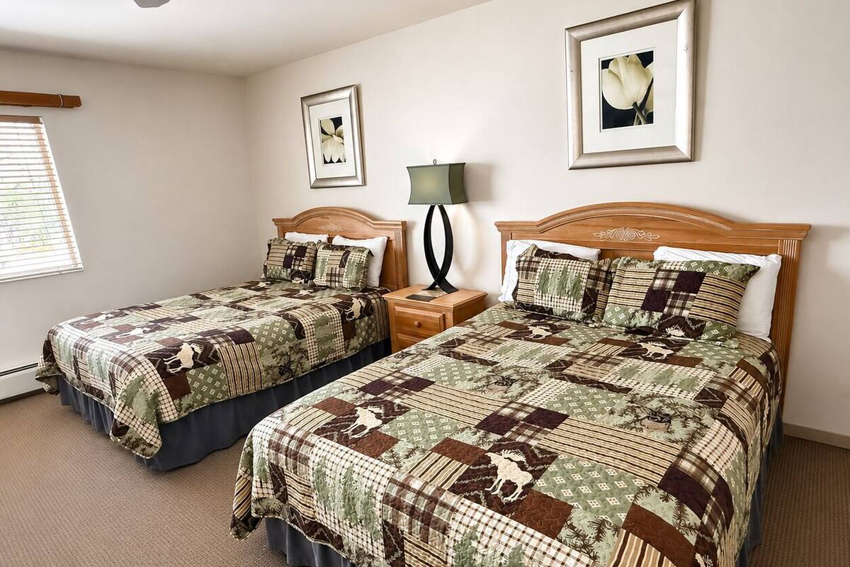 A double room with two beds, a ceiling fan, a nightstand with a lamp, and framed pictures on the wall.